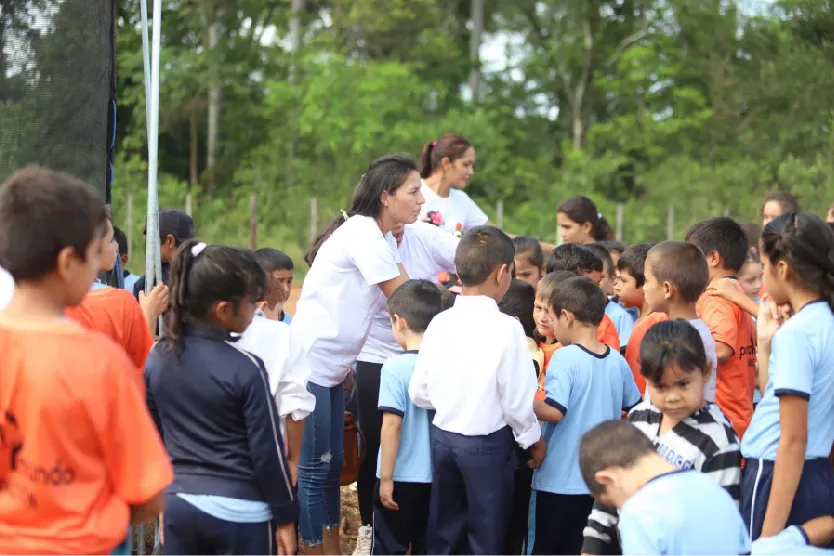 Una multitud de niños y adolescentes sonriend, en medio hay tres personas que están ayudando a educar a los niños